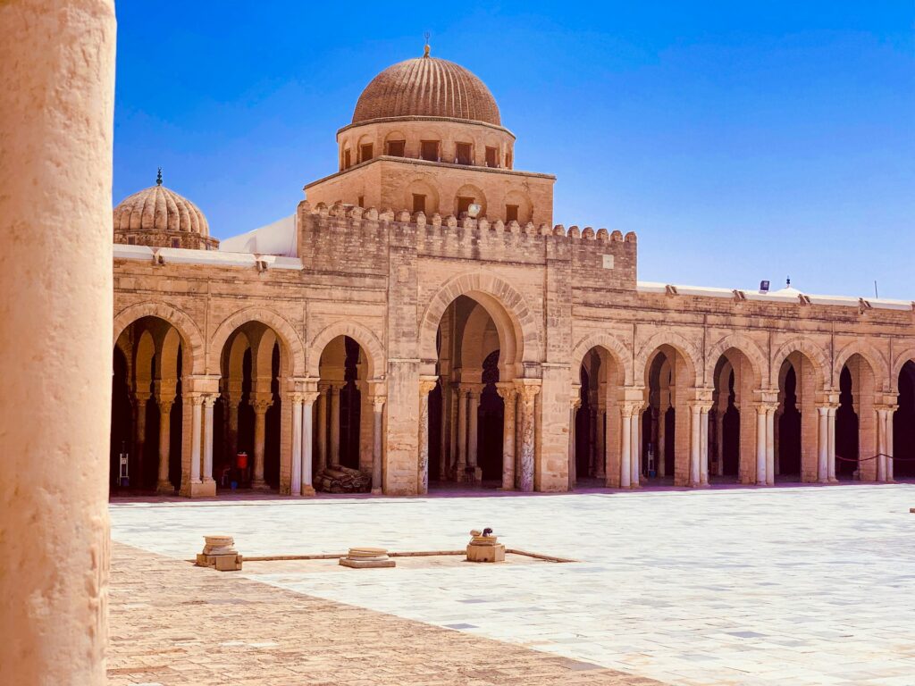 Ampio cortile interno della Grande Moschea di Kairouan, Tunisia, con il minareto a tre piani e il porticato sorretto da antiche colonne in marmo.