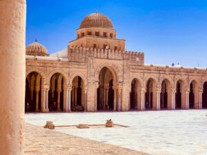 Ampio cortile interno della Grande Moschea di Kairouan, Tunisia, con il minareto a tre piani e il porticato sorretto da antiche colonne in marmo.